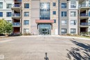 Contemporary multi-story building featuring a prominent glass-enclosed entrance, stone accents, multiple balconies with glass railings, and a varied facade of paneling and stucco - #404 12804 140 Av Nw, Edmonton, AB 