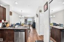 Kitchen featuring dark wood-finish cabinetry, stainless steel dishwasher, and a granite-style countertop island - #404 12804 140 Av Nw, Edmonton, AB 
