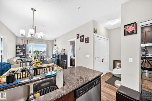 Open-concept living space with a kitchen island featuring a double-basin sink, a built-in dishwasher, and a stone-finish countertop - #404 12804 140 Av Nw, Edmonton, AB 