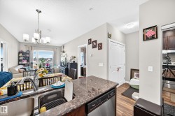 Open-concept living space with a kitchen island featuring a double-basin sink, a built-in dishwasher, and a stone-finish countertop - 