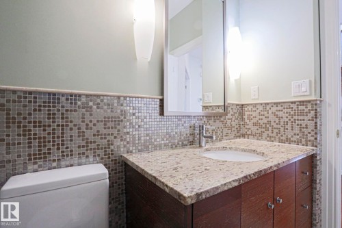 Granite countertop, wood-finish vanity, mosaic tile backsplash, rectangular medicine cabinet, and wall-mounted sconces - 995 Ogilvie Boulevard Nw, Edmonton, AB 