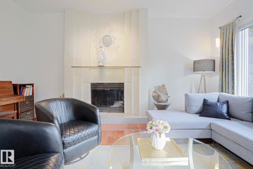 Fireplace with a decorative mantel and glass shelf, crown molding, wood-finish flooring, and natural light from a window - 995 Ogilvie Boulevard Nw, Edmonton, AB 