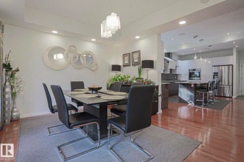 Recessed lighting illuminates the dining area with a contemporary chandelier, showcasing wood-finish flooring extending into the kitchen - 995 Ogilvie Boulevard Nw, Edmonton, AB 