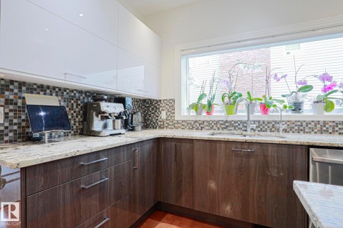 Contemporary kitchen featuring a corner sink, mosaic tile backsplash, under-cabinet lighting, and a large window - 995 Ogilvie Boulevard Nw, Edmonton, AB 