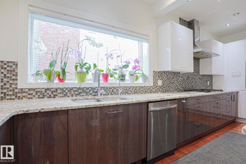 Expansive kitchen window, mosaic tile backsplash, granite countertops, wood-finish lower cabinetry, and stainless steel dishwasher - 995 Ogilvie Boulevard Nw, Edmonton, AB 