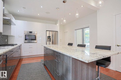 Kitchen featuring granite countertops, stainless steel appliances, white flat-panel cabinetry, a wood-finish island with integrated storage, and recessed lighting - 995 Ogilvie Boulevard Nw, Edmonton, AB 