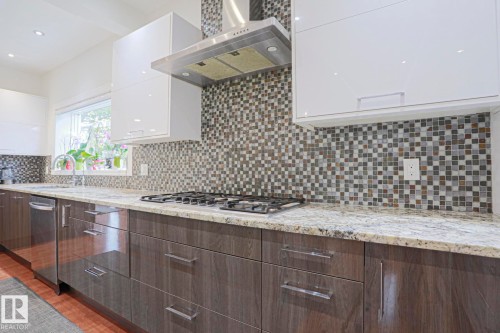 Kitchen featuring a gas cooktop, stainless steel range hood, mosaic tile backsplash, light-toned countertops, and wood-finish lower cabinetry - 995 Ogilvie Boulevard Nw, Edmonton, AB 