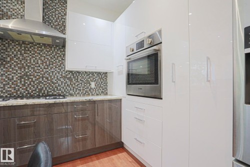 Modern kitchen with white and wood-finish cabinetry, stainless steel appliances, mosaic tile backsplash, and light-toned countertops - 995 Ogilvie Boulevard Nw, Edmonton, AB 