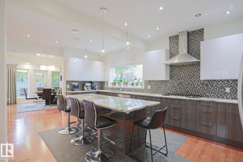 Spacious kitchen featuring an expansive island with a stone countertop, glossy white upper cabinetry, wood-finish lower cabinetry, and a mosaic tile backsplash - 995 Ogilvie Boulevard Nw, Edmonton, AB 