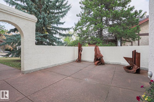 Private patio with textured stucco walls, an arched entryway, and mature perimeter trees - 995 Ogilvie Boulevard Nw, Edmonton, AB 