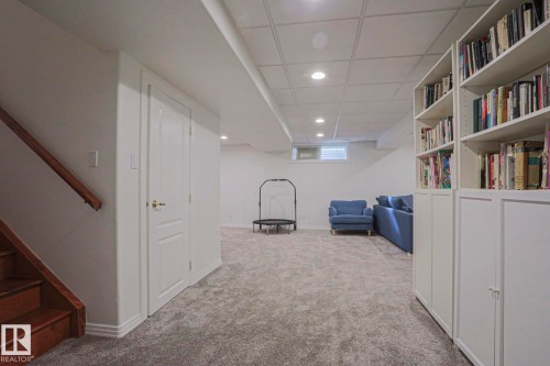 Finished lower level with recessed lighting, plush carpeting, built-in shelving, and a wood staircase with railing - 995 Ogilvie Boulevard Nw, Edmonton, AB 