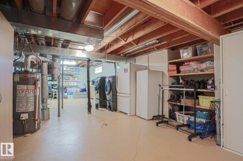 Finished basement space featuring exposed wood beams, built-in shelving, two white refrigerators, and a water heater - 995 Ogilvie Boulevard Nw, Edmonton, AB 