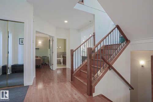 Hardwood flooring throughout the hallway, wood staircase with metal balusters, recessed lighting, mirrored closet doors, and sconce lighting - 995 Ogilvie Boulevard Nw, Edmonton, AB 