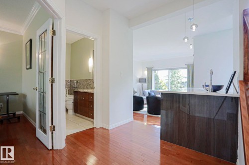 Hardwood flooring throughout, a bathroom with vanity and granite countertop, and a kitchen island with a white countertop and built-in sink - 995 Ogilvie Boulevard Nw, Edmonton, AB 
