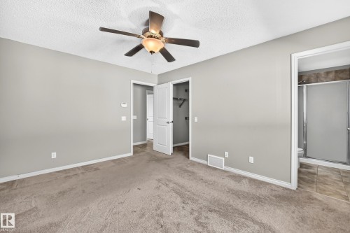 Neutral-toned carpeting and walls, overhead ceiling fan with lighting, white trim, and doors, with an adjacent bathroom featuring a tiled shower enclosure - 21 Silverstone Drive, Stony Plain, AB 