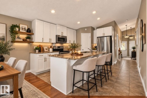 Kitchen featuring white cabinetry, stainless steel appliances, a center island with seating, and wood-finish flooring - 21 Silverstone Drive, Stony Plain, AB 