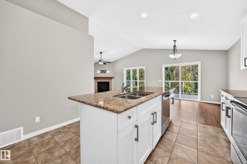 Kitchen island with a double basin sink, stone-finish countertop, and white cabinetry - 21 Silverstone Drive, Stony Plain, AB 