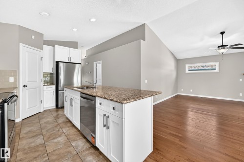 Kitchen island with granite countertop, white cabinetry, stainless steel appliances, and tile flooring - 21 Silverstone Drive, Stony Plain, AB 