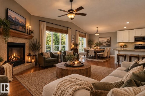 Vaulted ceiling featuring a ceiling fan, stone-clad fireplace with wood mantel, large windows with natural wood blinds, wood-finish flooring, and a kitchen with white cabinetry and stainless steel appliances - 21 Silverstone Drive, Stony Plain, AB 