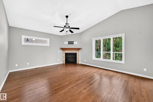 Vaulted ceiling with a ceiling fan, a corner fireplace with a wood mantel, wood-finish flooring, and large windows - 21 Silverstone Drive, Stony Plain, AB 