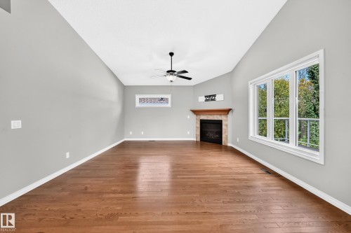 Vaulted ceiling, wood-finish flooring, built-in fireplace with a wood mantle, ceiling fan, and large windows - 21 Silverstone Drive, Stony Plain, AB 