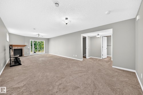 Expansive carpeted living space featuring a fireplace with a wood mantel, sliding glass doors, recessed lighting, and a white interior door - 21 Silverstone Drive, Stony Plain, AB 