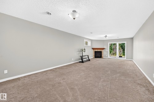 Spacious room featuring carpeting, a fireplace with a wood mantle, a window, and sliding glass doors to the exterior - 21 Silverstone Drive, Stony Plain, AB 