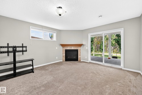 Room featuring a tiled fireplace with wood mantel, carpet flooring, a horizontal transom window, and sliding glass doors leading to an outdoor space - 21 Silverstone Drive, Stony Plain, AB 