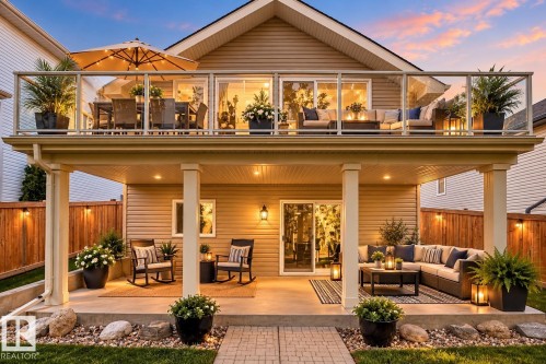 Expansive dual-level outdoor living space with an upper deck featuring glass panel railing and a lower covered patio with recessed lighting - 21 Silverstone Drive, Stony Plain, AB 