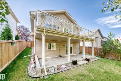 Expansive backyard featuring a manicured lawn, full fencing, a concrete patio, and an upper-level deck with a glass railing - 21 Silverstone Drive, Stony Plain, AB 