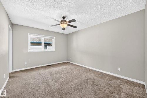 Neutral tone wall paint, textured ceiling, ceiling fan with integrated lighting, window with white trim, and carpet flooring - 21 Silverstone Drive, Stony Plain, AB 
