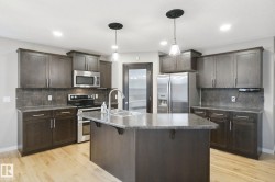 Kitchen featuring wood-finish flooring, dark wood cabinetry, stainless steel appliances, a center island with a double basin sink, and pendant lighting - 