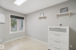Recessed ceiling light fixture, neutral wall paint, wood-finish flooring, white window trim, and a black window blind - 
