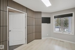 Light wood-finish flooring, accent wall with vertical slat paneling, mounted television, and a double-hung window - 
