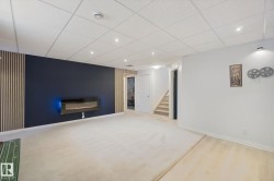 Spacious room featuring a wall-mounted electric fireplace, recessed lighting, and a drop ceiling - 