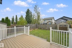 Expansive backyard featuring a composite deck, white railing, manicured lawn, and raised garden beds - 