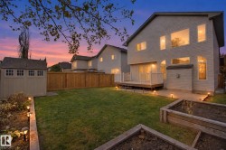 Spacious backyard oasis featuring a manicured lawn, raised garden beds, mature tree canopy, and ambient landscape lighting - 