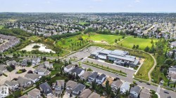 Expansive residential area featuring numerous single-family homes, a large green space with a pond, and a community building with an adjacent parking area - 