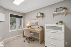 Bright home office featuring a wood-finish desk, upholstered task chair, white three-drawer dresser with integrated storage, and floating wooden shelves with potted plants - 