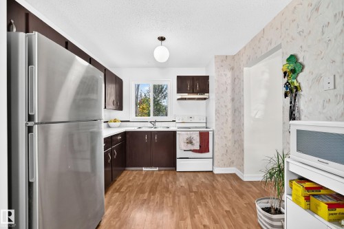 Kitchen featuring wood-finish flooring, dark wood-finish cabinetry, white countertops, and white appliances - 11007 173A Avenue Nw, Edmonton, AB 