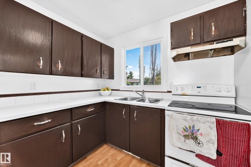 Kitchen featuring dark-finish cabinetry, white countertops, a double basin sink, white tile backsplash, and wood-finish flooring - 11007 173A Avenue Nw, Edmonton, AB 