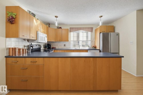 Kitchen featuring wood-finish cabinetry, a white tile backsplash, dark countertops, and stainless steel appliances - 17072 67 Avenue Nw, Edmonton, AB 