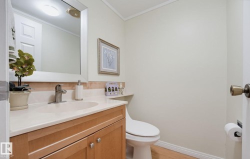 Light wood-finish flooring, a wood-finish vanity with an integrated sink, a large wall mirror, and a modern toilet - 17072 67 Avenue Nw, Edmonton, AB 