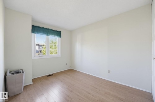Wood-finish flooring with white baseboards, bright white walls, and a window with white trim - 17072 67 Avenue Nw, Edmonton, AB 