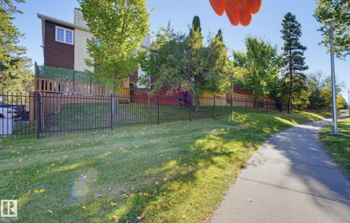 Exterior featuring a paved pathway, established trees, and a black wrought-iron fence - 17072 67 Avenue Nw, Edmonton, AB 