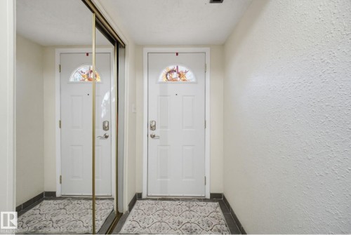 Entryway featuring a white paneled door with a decorative transom, a full-length mirrored closet, and tile flooring - 17072 67 Avenue Nw, Edmonton, AB 