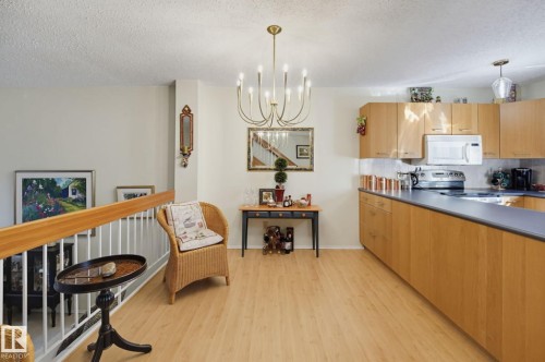 Wood-finish flooring, staircase with wood railing, recessed kitchen appliances, light wood-finish cabinetry, and a multi-arm chandelier - 17072 67 Avenue Nw, Edmonton, AB 