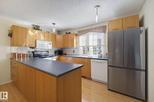 Kitchen featuring wood-finish cabinetry, dark countertops, a built-in microwave, and stainless steel appliances - 17072 67 Avenue Nw, Edmonton, AB 