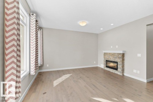 Stone-clad fireplace with a white mantel, wood-finish flooring, recessed lighting, and a flush mount ceiling fixture - 1523 168 Street Sw, Edmonton, AB 