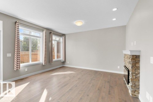 Engineered wood flooring, stone-clad fireplace, recessed lighting, double-pane windows, and light neutral wall tones - 1523 168 Street Sw, Edmonton, AB 